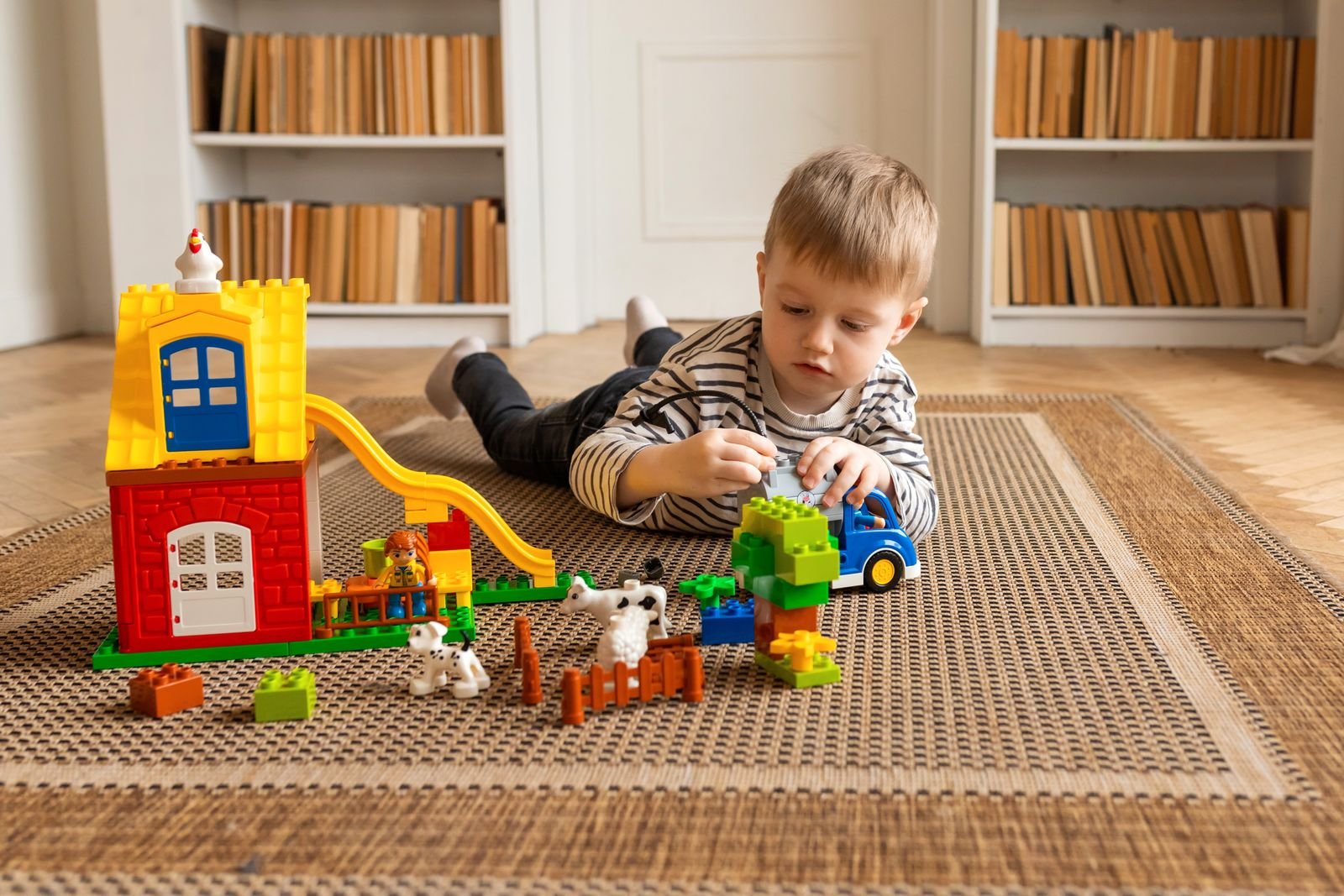 A boy lying on a carpet, playing with toys